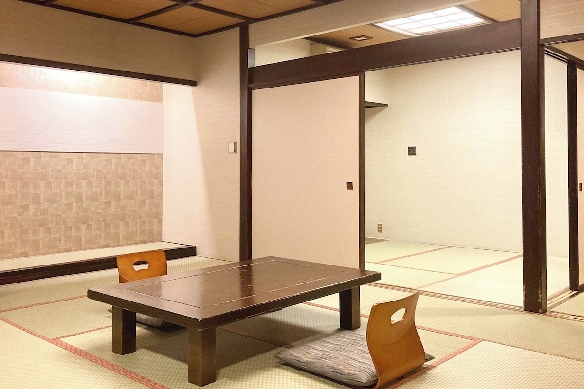A traditional Japanese room with tatami flooring, a low table, and two wooden chairs.