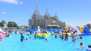Una piscina con gente y juguetes inflables, rodeada por un edificio de estilo arquitectónico particular.