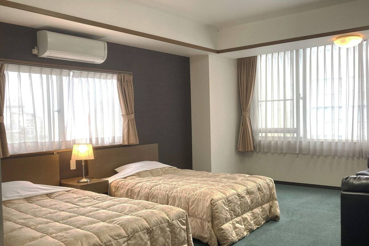 A hotel room with two beds, a desk, a chair, and an air conditioning unit.