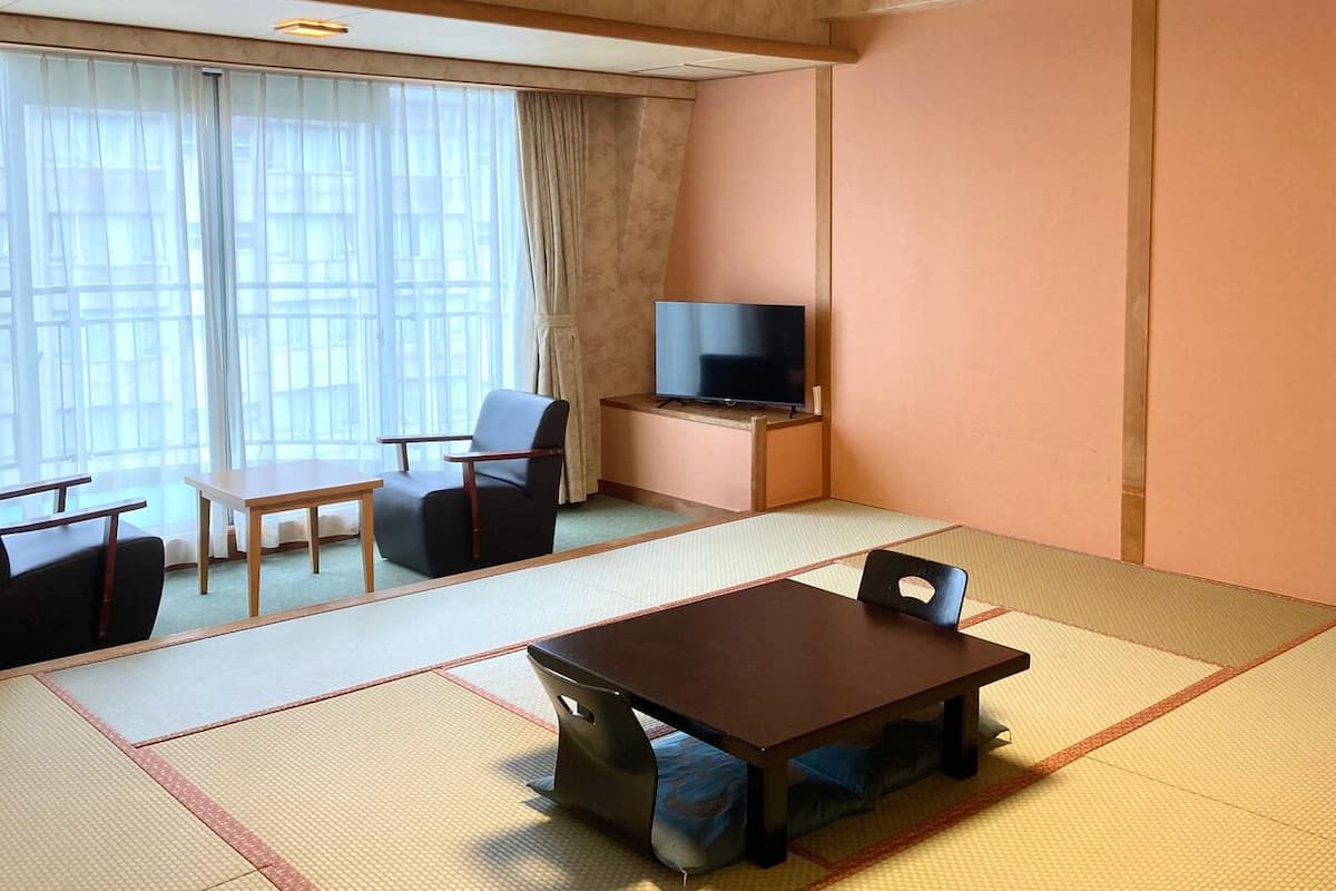 A room with tatami flooring, a television on a stand, a table, and chairs.