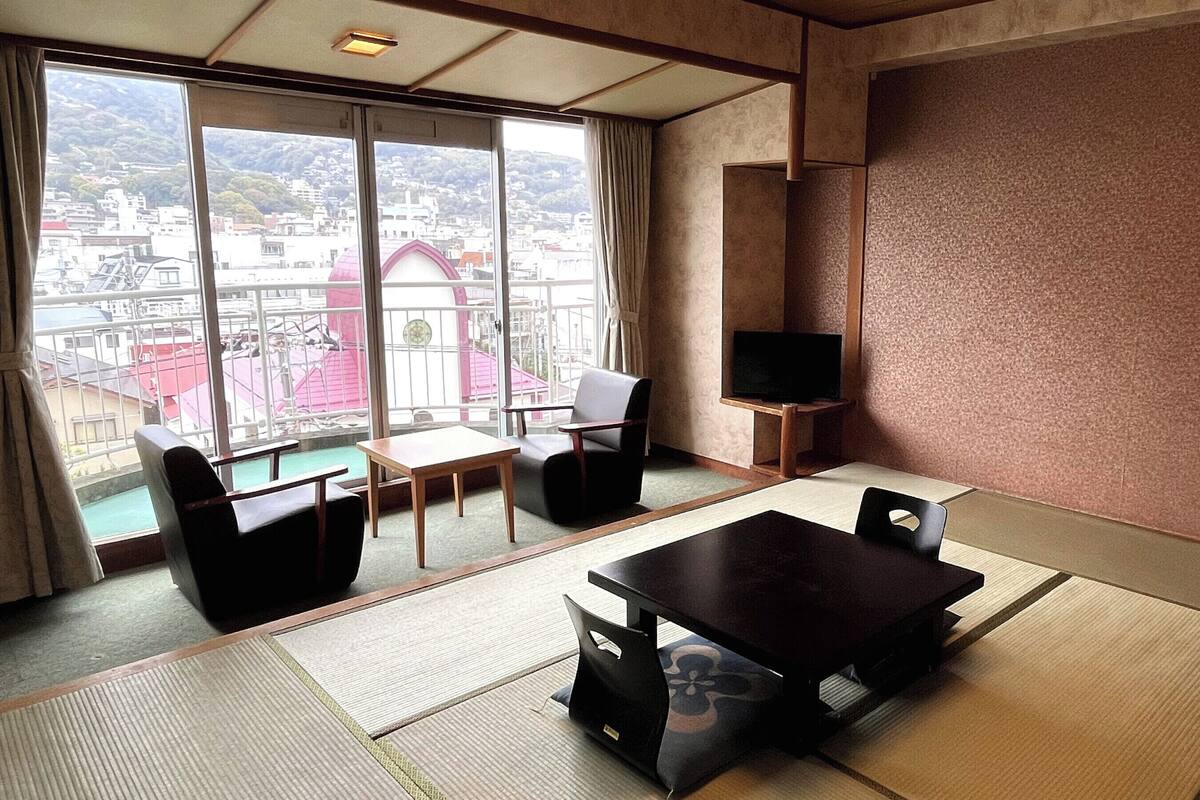 A room with tatami flooring, a television, a table, and chairs.