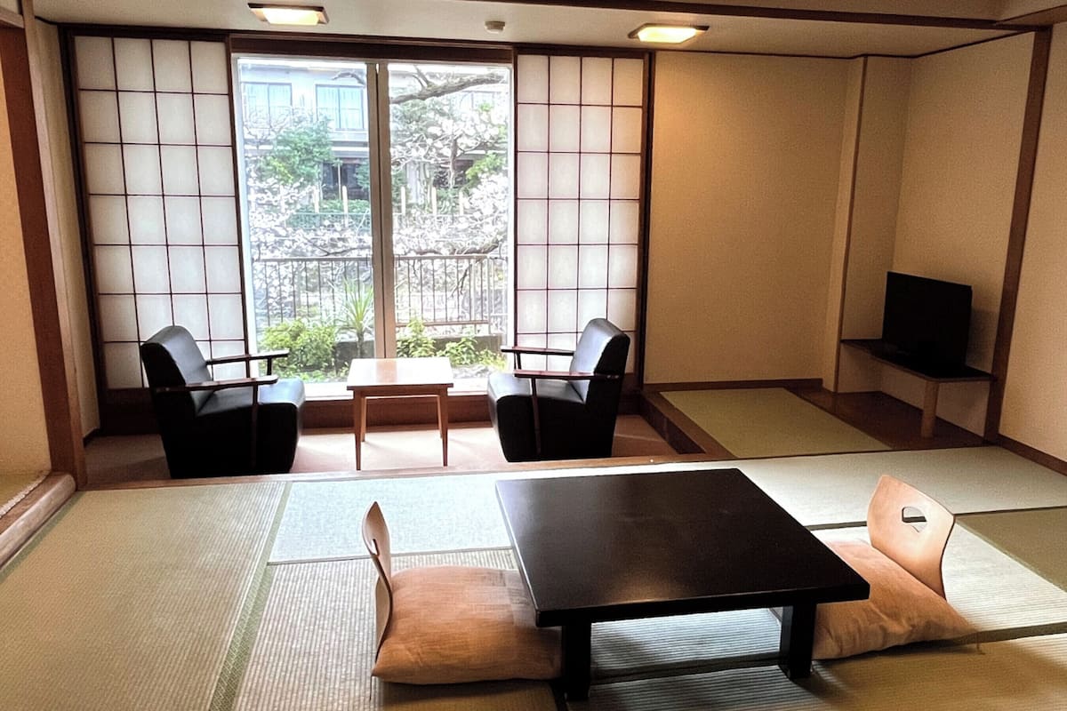 A traditional Japanese room with tatami flooring, a low table, two chairs, a sofa, and a television.