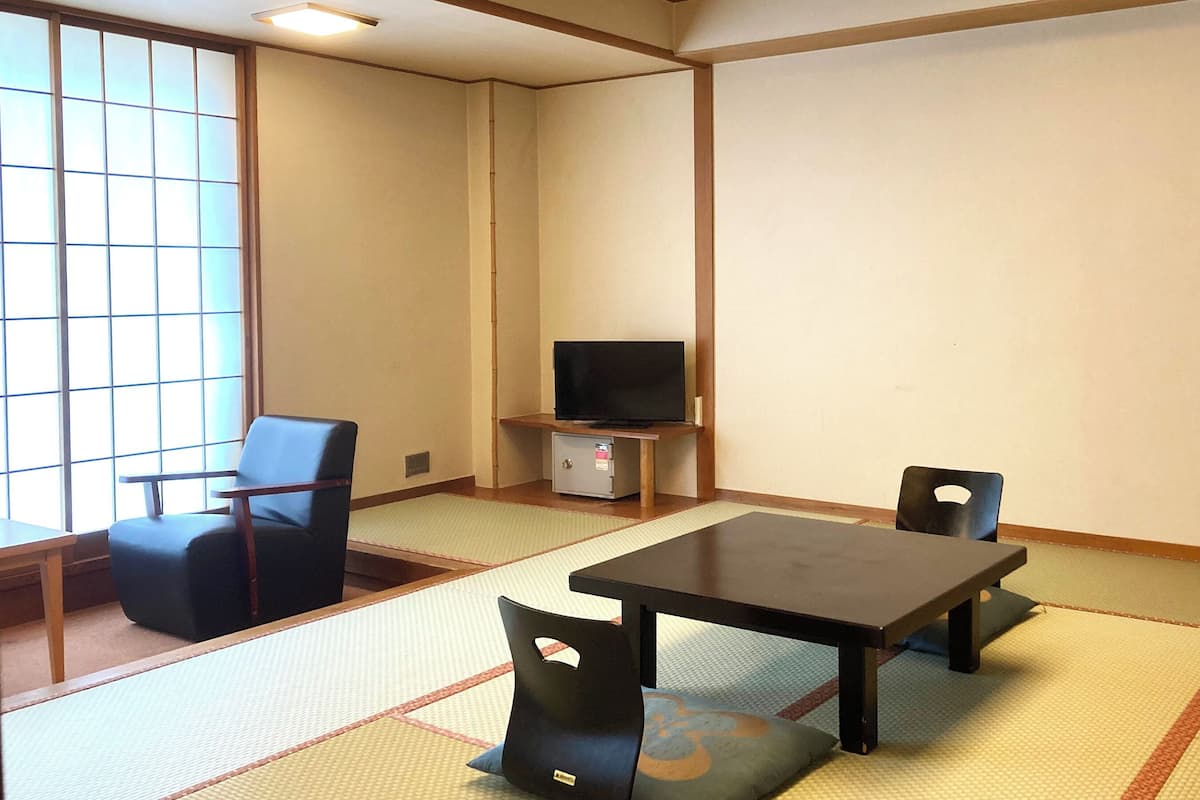 A room with tatami flooring, a low table with chairs, a television on a stand, and a sliding door.