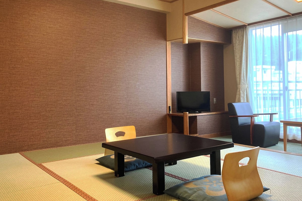 A hotel room with tatami flooring, a television, a dining table, and a chair.