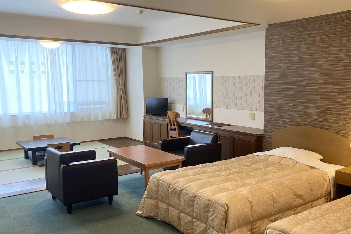 A hotel room with two beds, a desk, a chair, a TV, and a window with curtains.