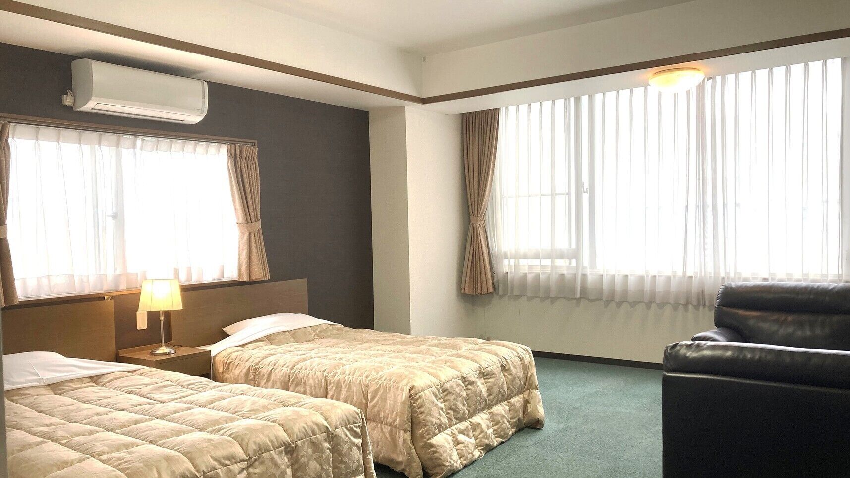 A hotel room with two beds, a chair, a desk, and a window with curtains.