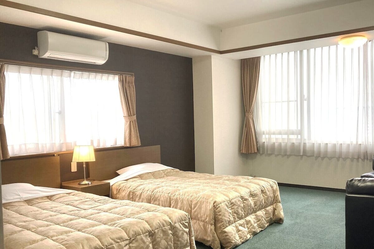 A hotel room with two beds, a chair, a desk, and a window with curtains.