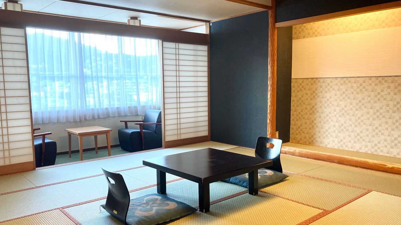 A tatami mat room with a low table and chairs, a sliding door, and a view through a large window.