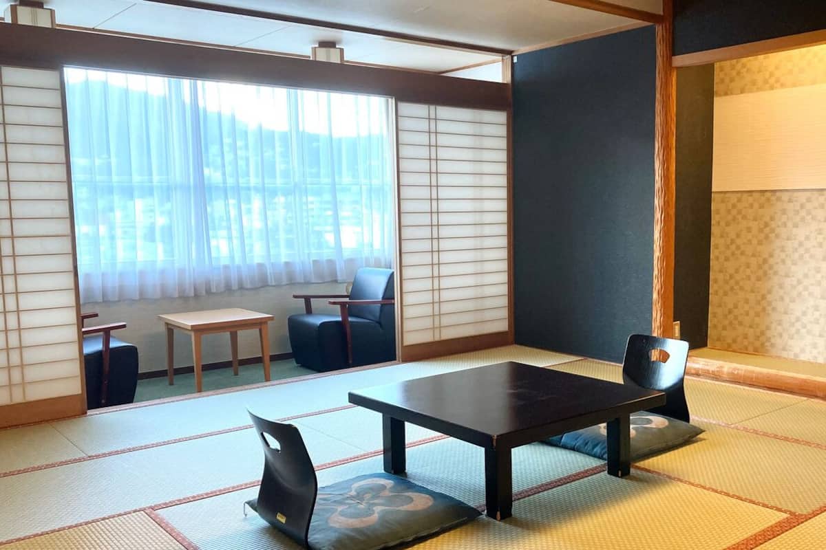 A tatami mat room with a low table and chairs, a sliding door, and a view through a large window.