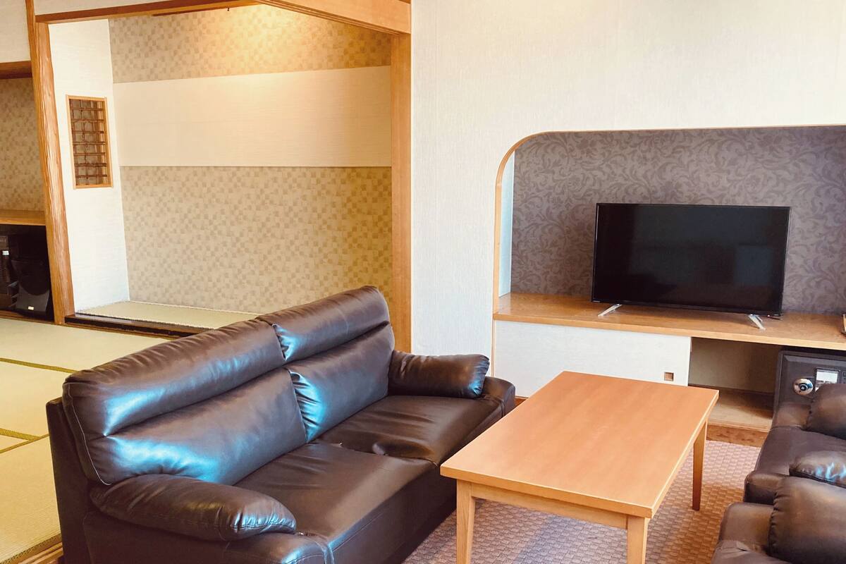 A living room with a sofa, a coffee table, a TV, and a patterned wall.