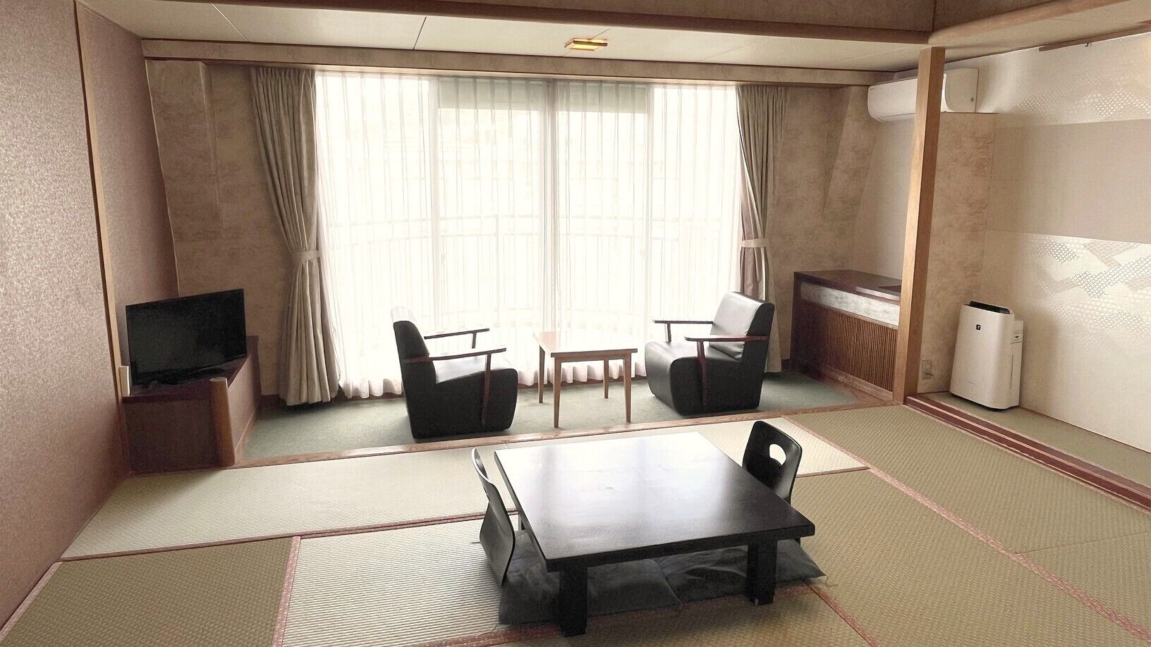 A room with tatami flooring, a table, two chairs, a television, and a radiator.