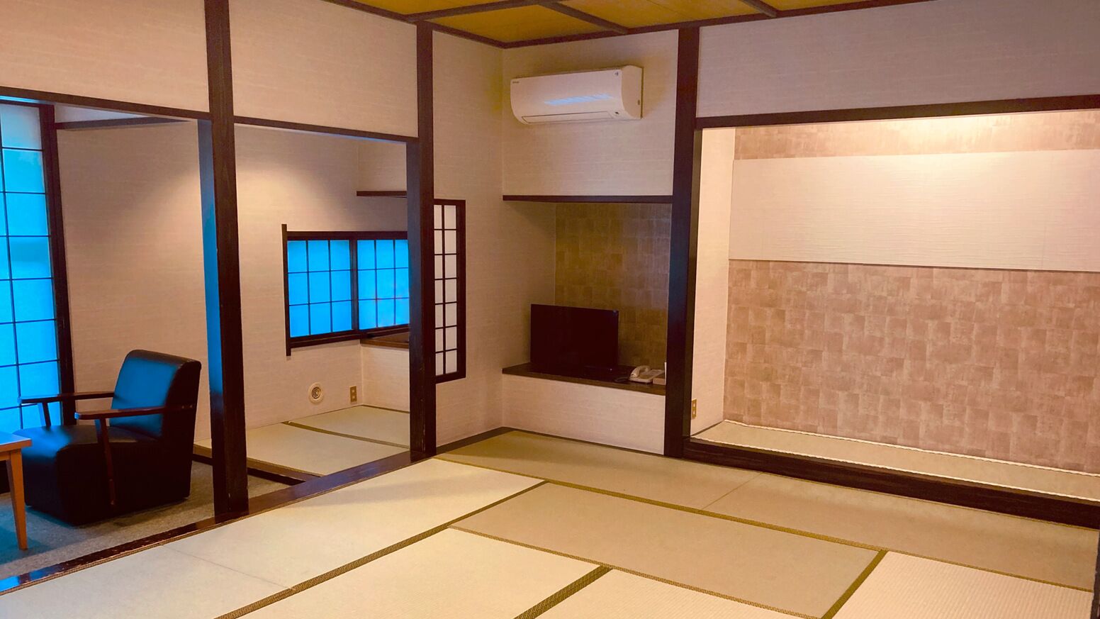 A traditional Japanese room with tatami flooring, a black chair, a sliding door, and a built-in shelf.