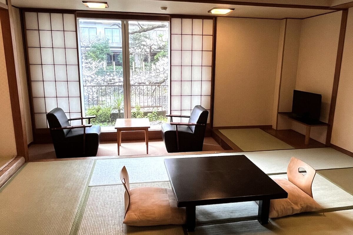 A traditional Japanese room with tatami flooring, a low table, two chairs, and a TV.