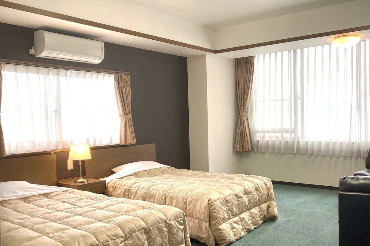 A hotel room with two beds, a chair, a desk, and a window with curtains.