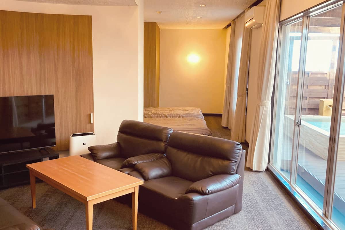 A living room with a sofa, a TV, a wooden table, and a sliding glass door leading to a balcony.