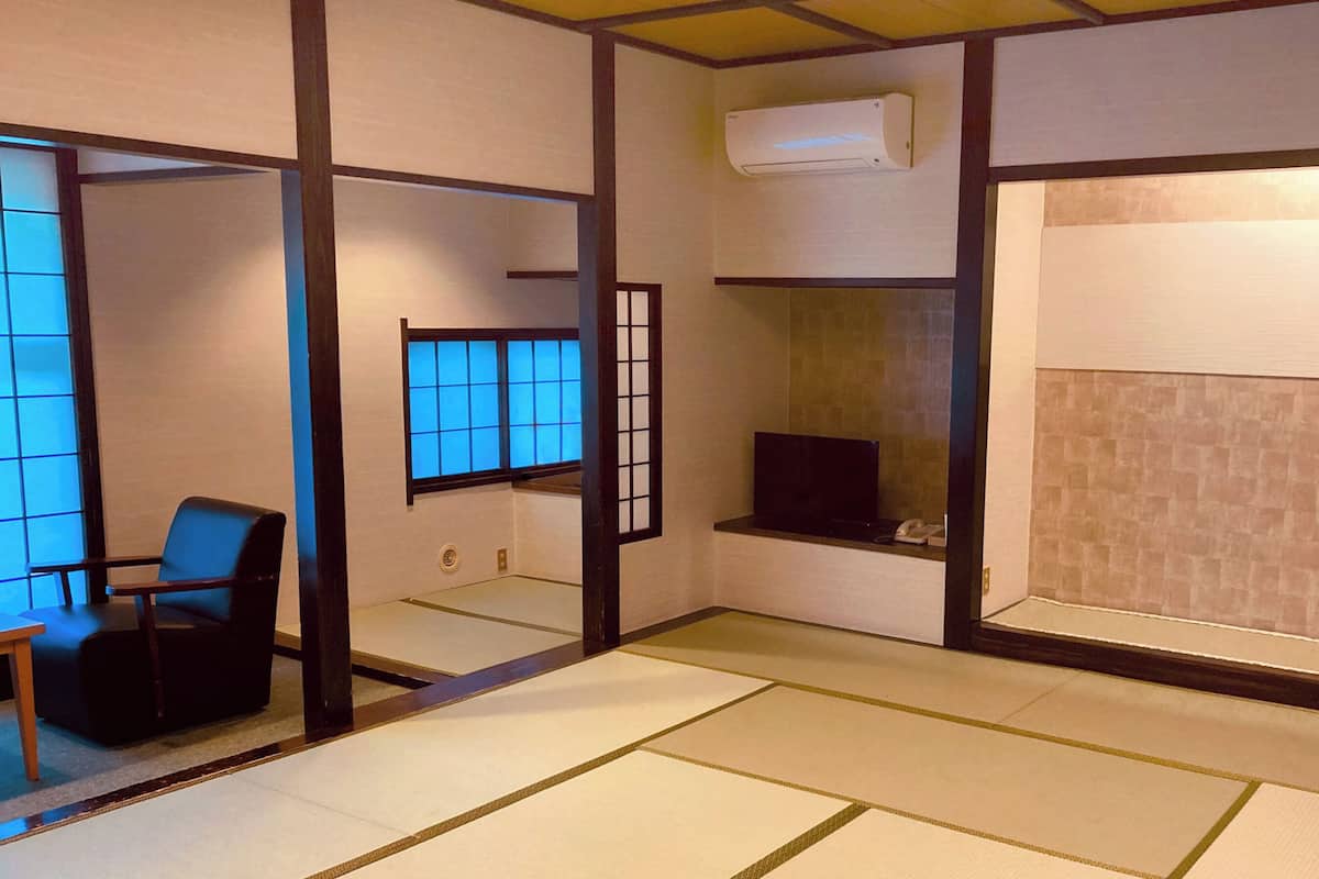 A traditional Japanese room with tatami flooring, a sliding door, a black chair, a TV, and an air conditioning unit.