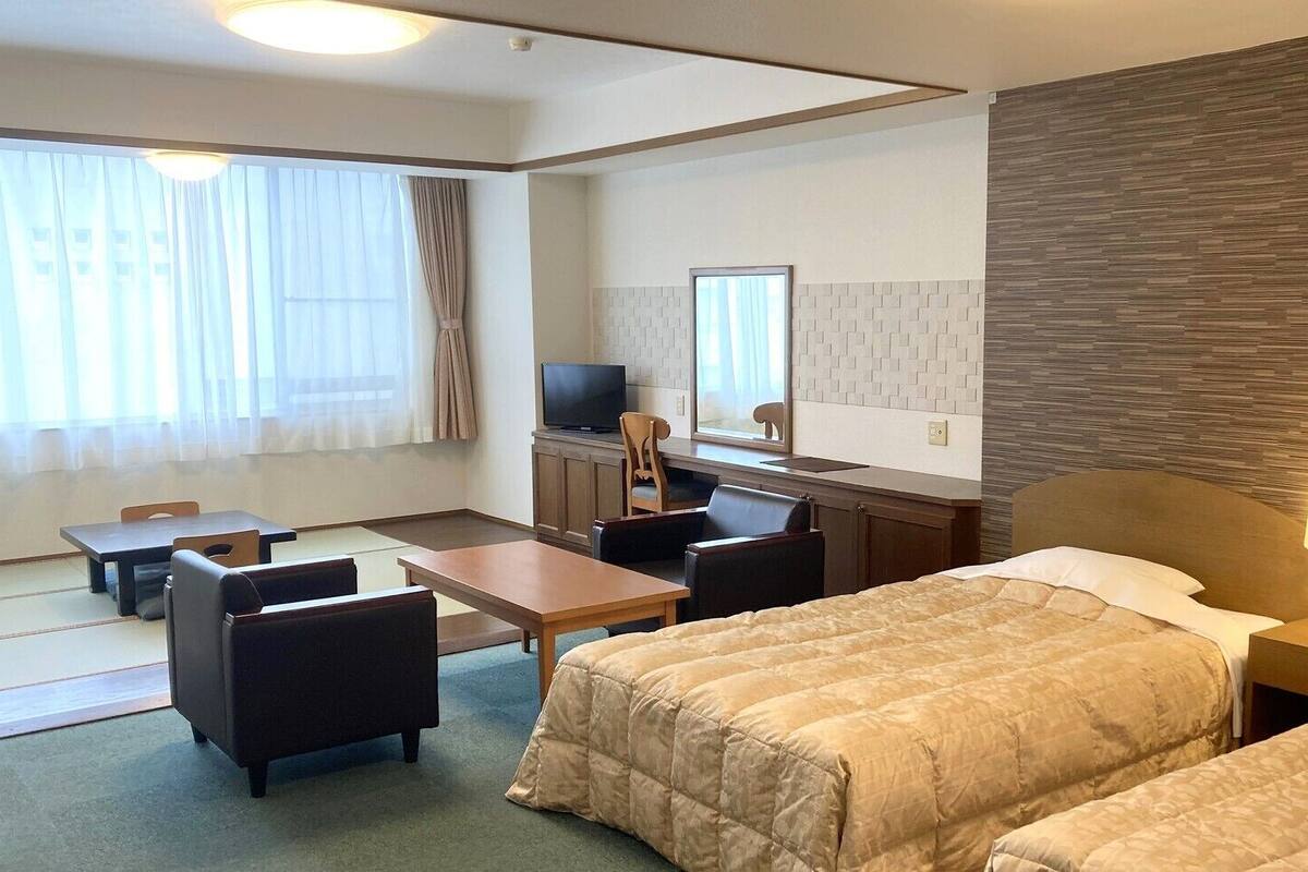 A hotel room with a bed, a desk, a chair, a television, and a lamp.