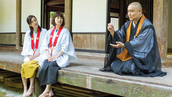 Three individuals seated on a wooden bench outside a building with traditional architecture.