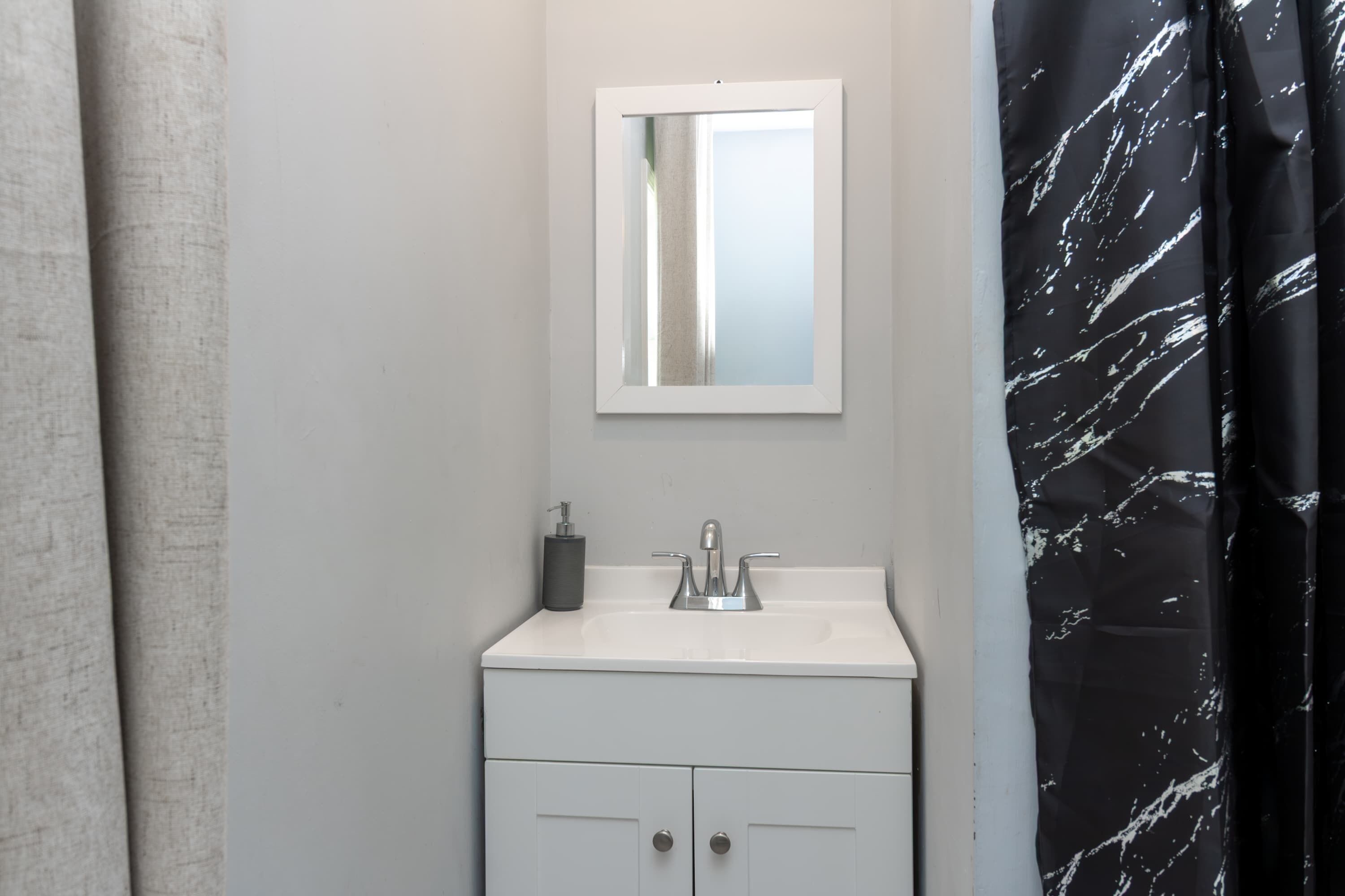 A bathroom with a white sink, a mirror, and a black and white patterned shower curtain.