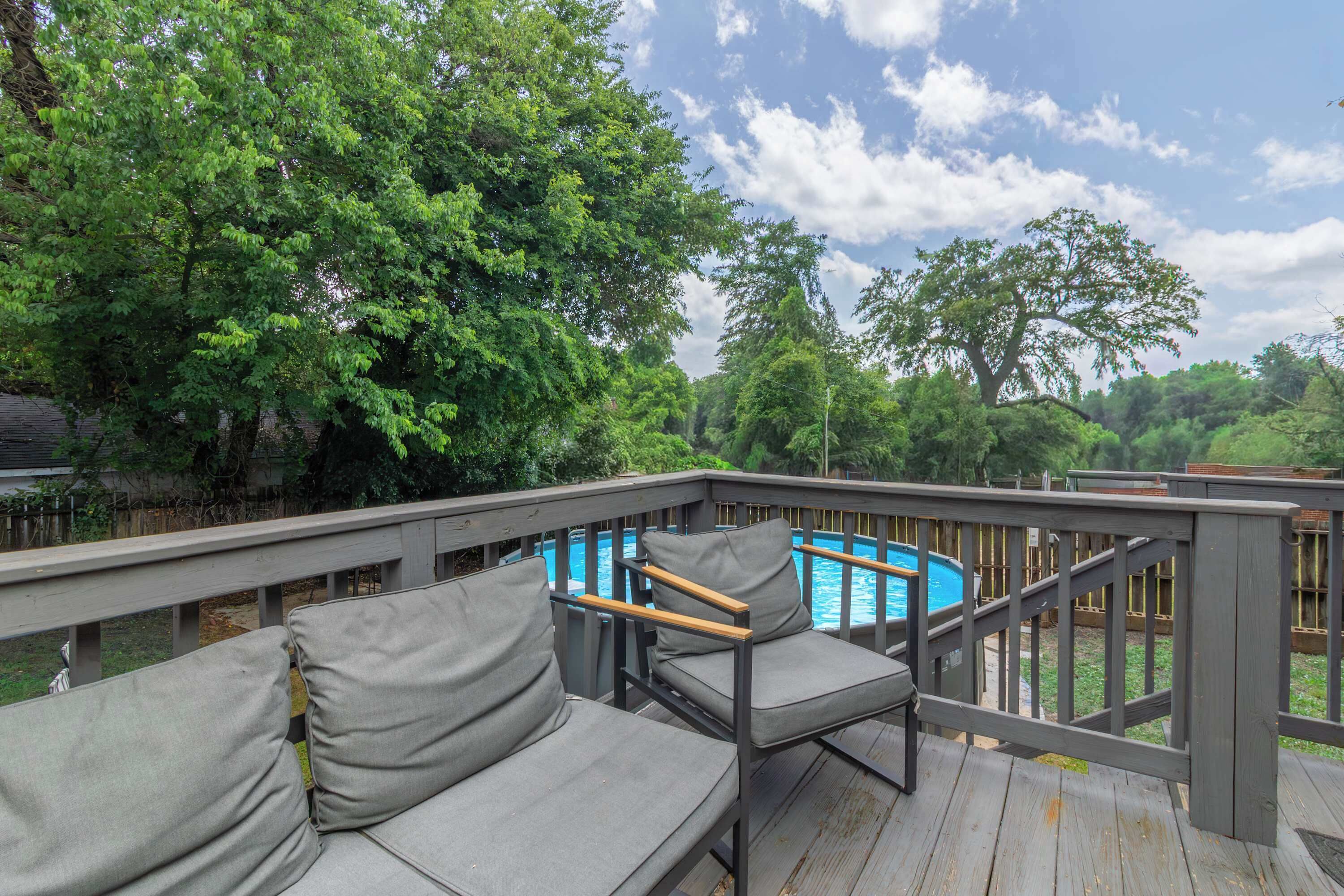 A deck with a pool, surrounded by trees, and includes a sofa and chairs.