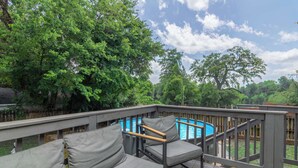 Eine Poolterrasse, umgeben von Bäumen, mit einer Sitzecke und Liegestühlen.