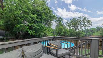 A deck with a pool, surrounded by trees, and includes a sofa and chairs.