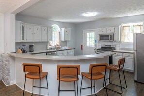 A kitchen with white cabinets, a central island with bar stools, a microwave, stove, and a refrigerator. - Ultimate Group Stay with Private Pool: Sleeps 18 Near Riverwalk (Columbus)