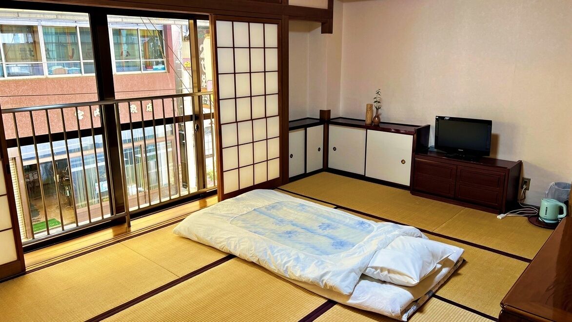 A traditional Japanese room with tatami flooring, a futon bed, sliding doors, a television, and a cabinet.
