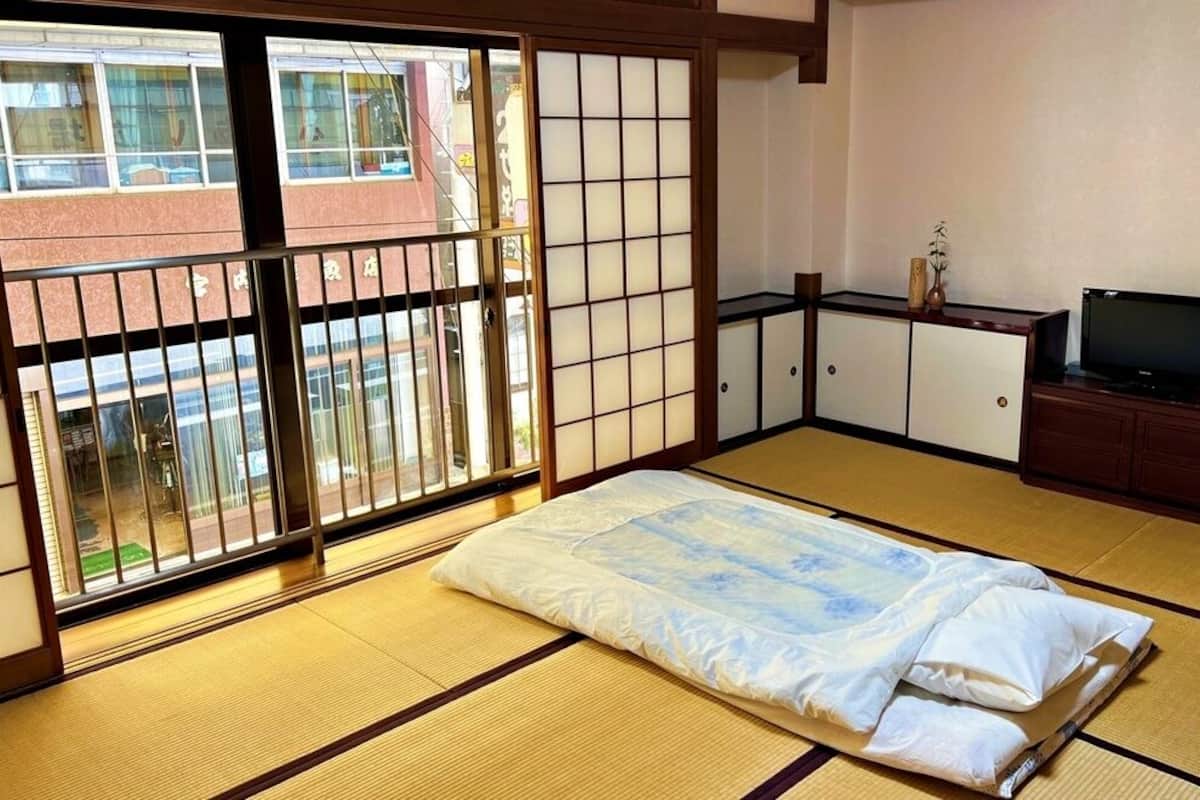 Ett traditionellt japanskt rum med tatamimattor på golvet, en futonmadrass, skjutdörrar, en tv och ett skåp.