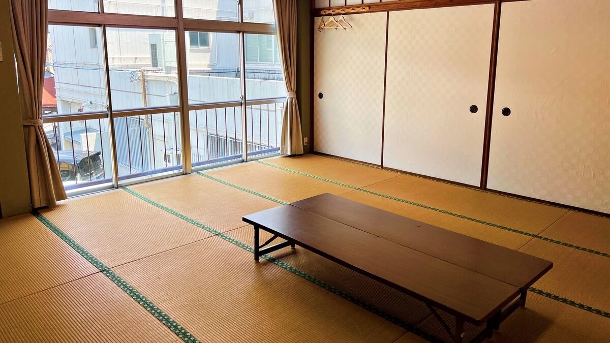 A tatami mat room with a sliding door, a tatami mat table, and a view through a large window.