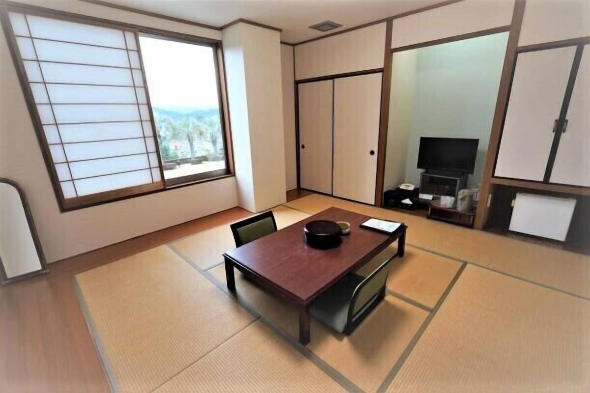 A room with tatami flooring, a wooden table, a television, and sliding doors.