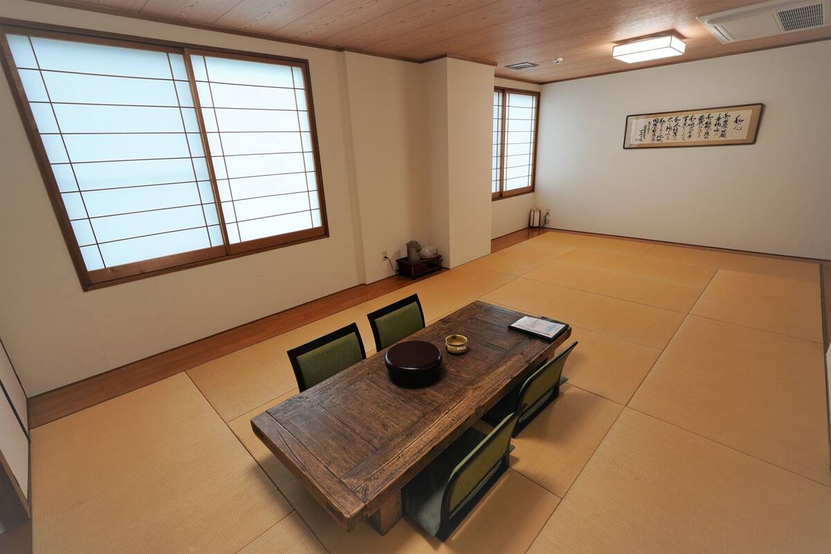 A traditional Japanese room with tatami flooring, a wooden dining table, green chairs, and sliding shoji doors.