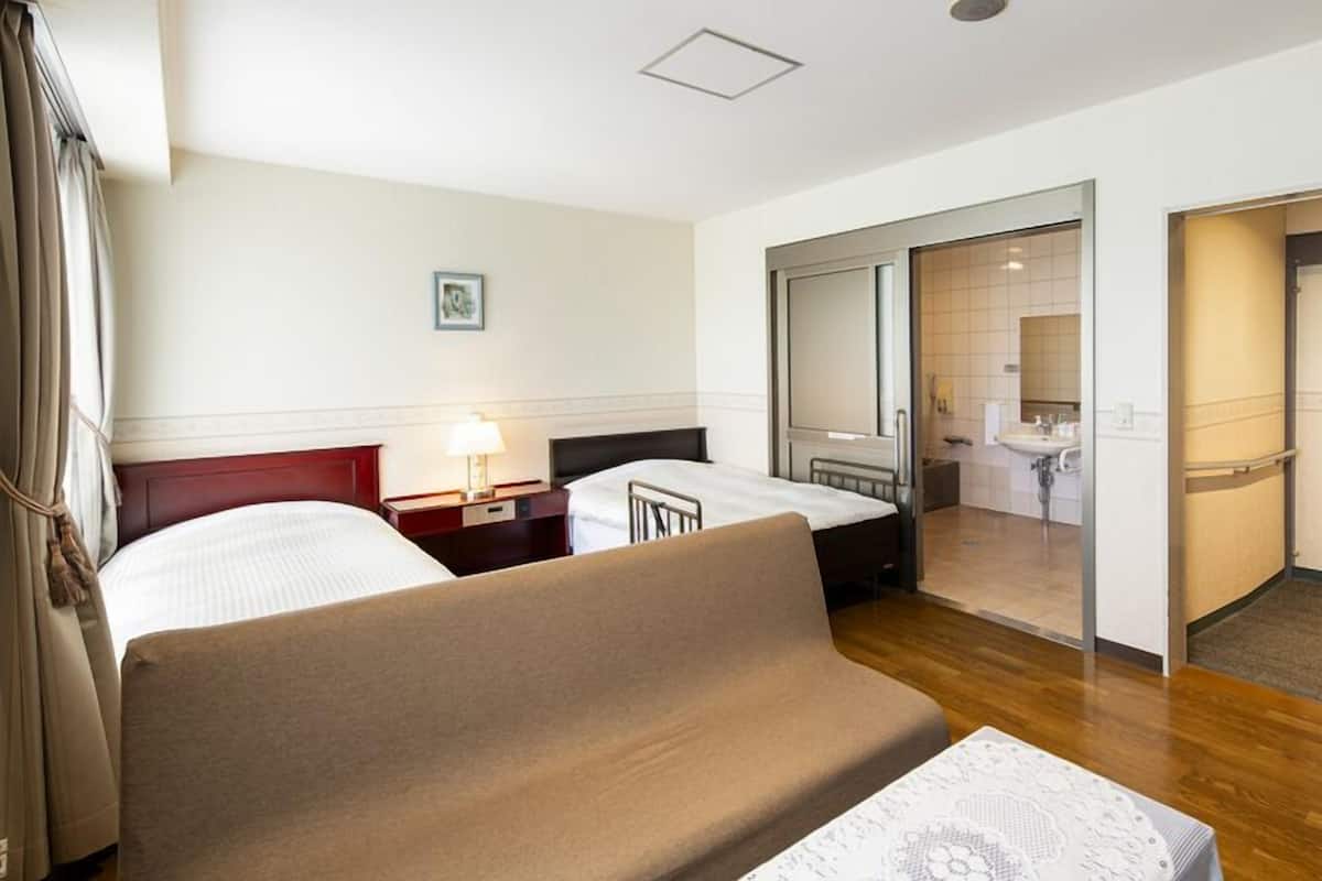 A hotel room with a large bed, bedside tables, a lamp, a mirror, and a bathroom visible through an open door.