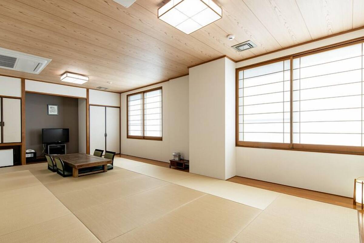 A traditional Japanese room with tatami flooring, a low wooden table, a television, sliding doors, and large windows.