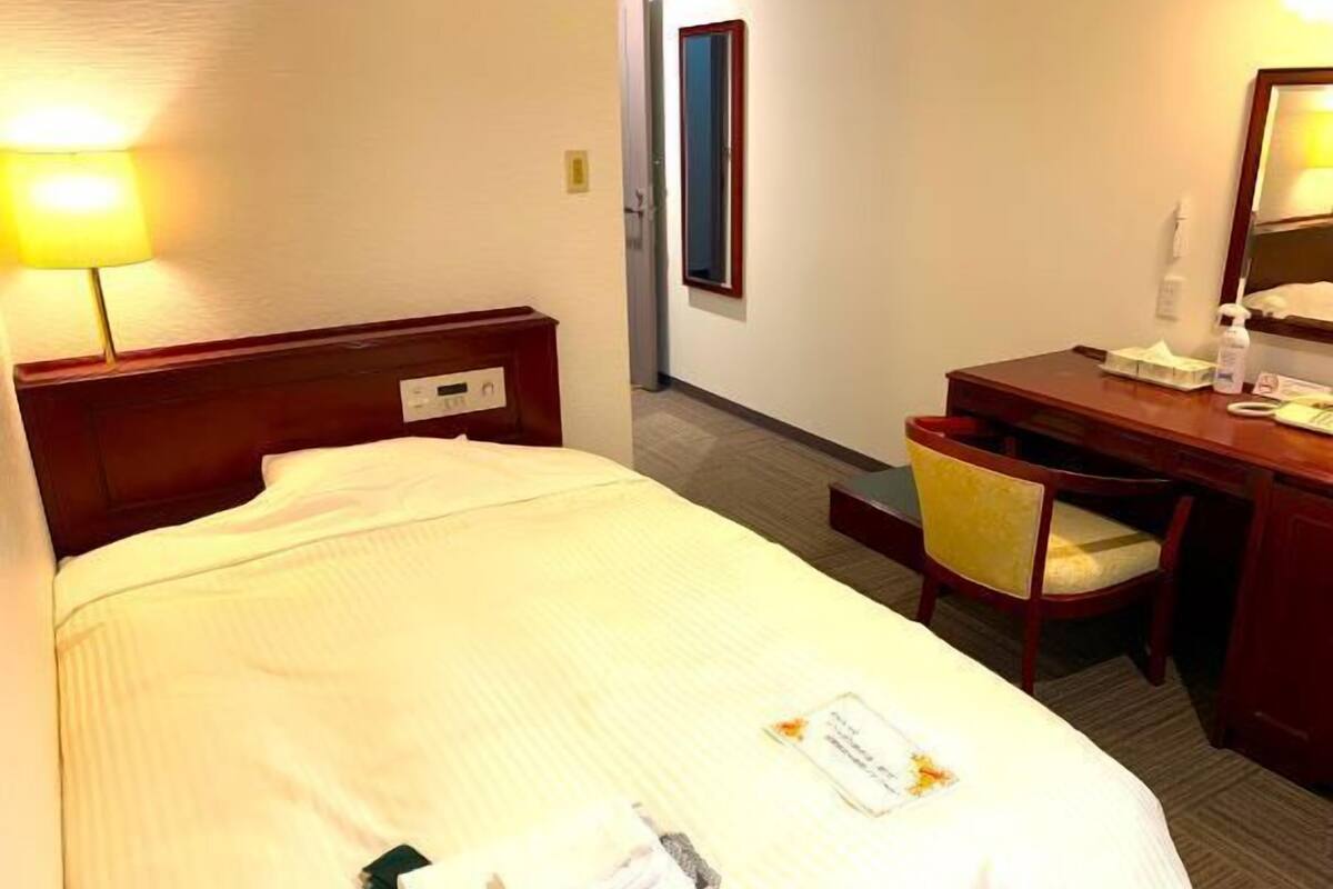 A hotel room with a bed, bedside table, chair, desk, and lamp.