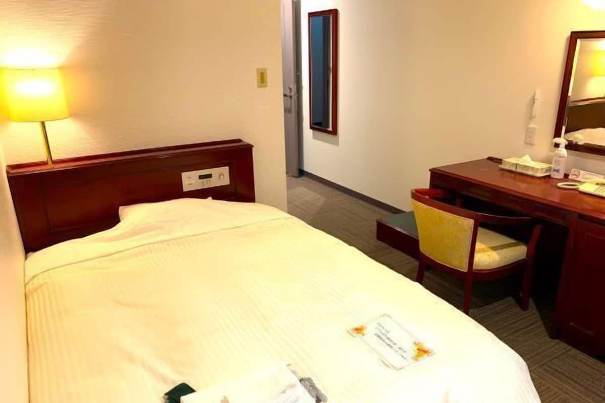 A hotel room with a bed, bedside table, chair, desk, and lamp.