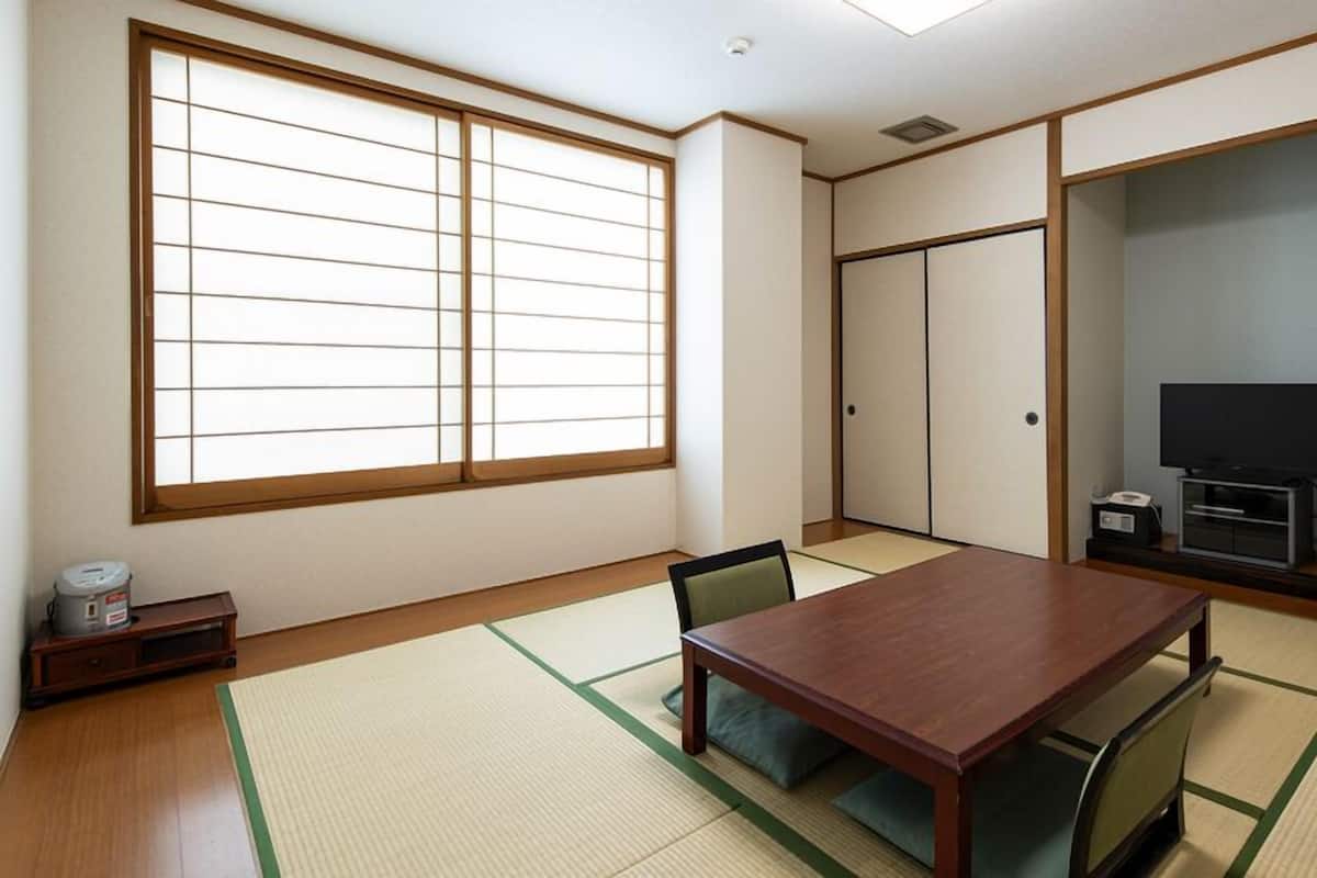 A traditional Japanese room with tatami flooring, a wooden table, a television, and sliding doors.