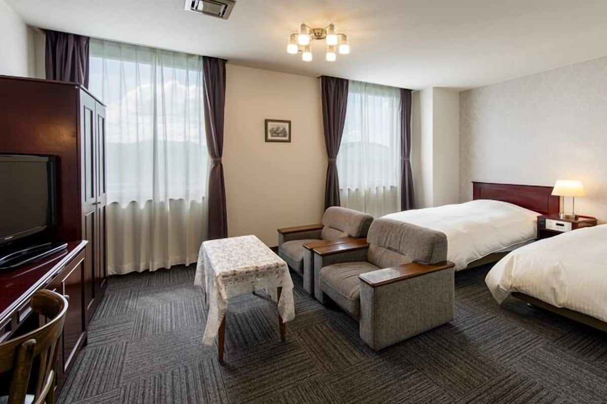 A hotel room with two beds, a TV, a desk, a chair, and a small table.