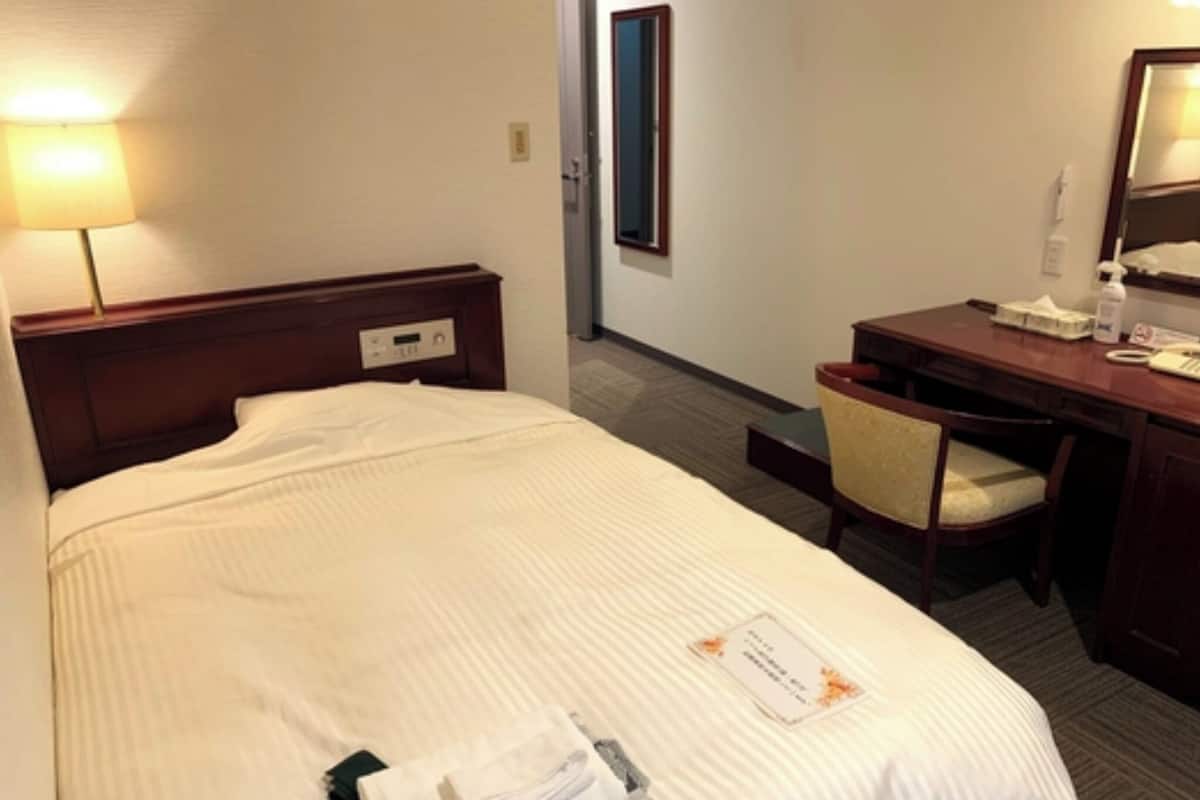 A hotel room with a bed, a desk, a chair, and a lamp.