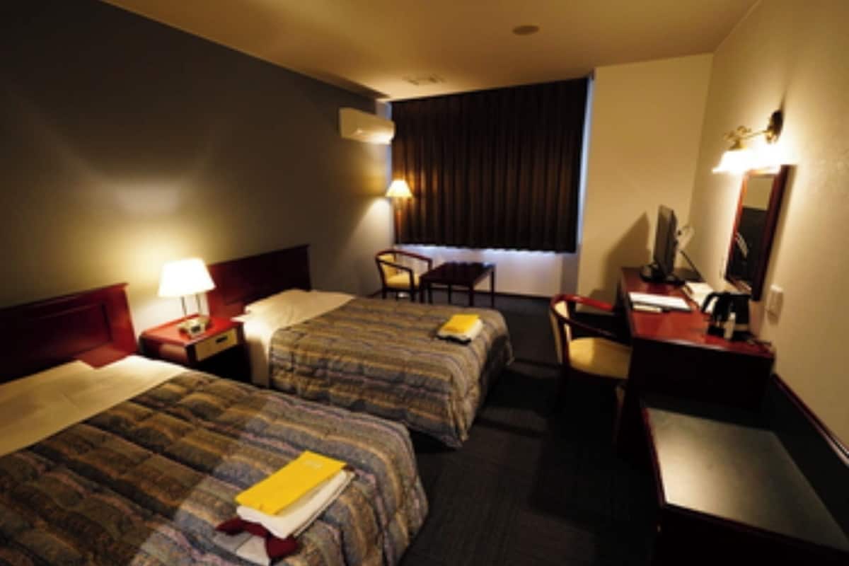 A hotel room with two beds, a desk, a chair, a desk lamp, and a television.