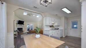 A spacious living area with a dining table, a TV mounted on the wall, and a kitchen with white cabinets. - Near the Hospital and Dining - Sunrise Knoll Stay (Columbus)