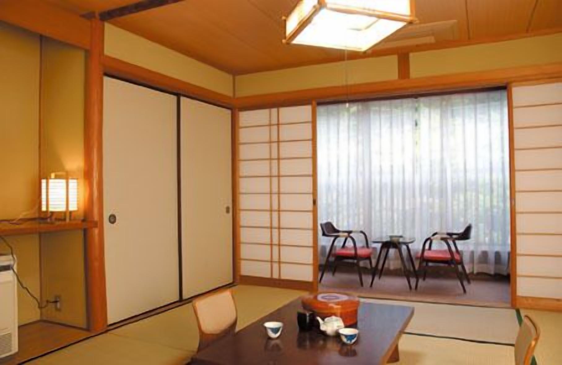 A traditional Japanese room with tatami flooring, a low table with tea set, sliding doors, and a view through a shoji screen.