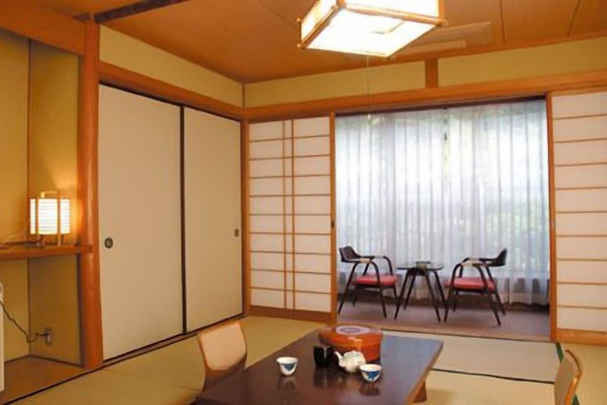 A traditional Japanese room with tatami flooring, a low table with tea set, sliding doors, and a view through a shoji screen.