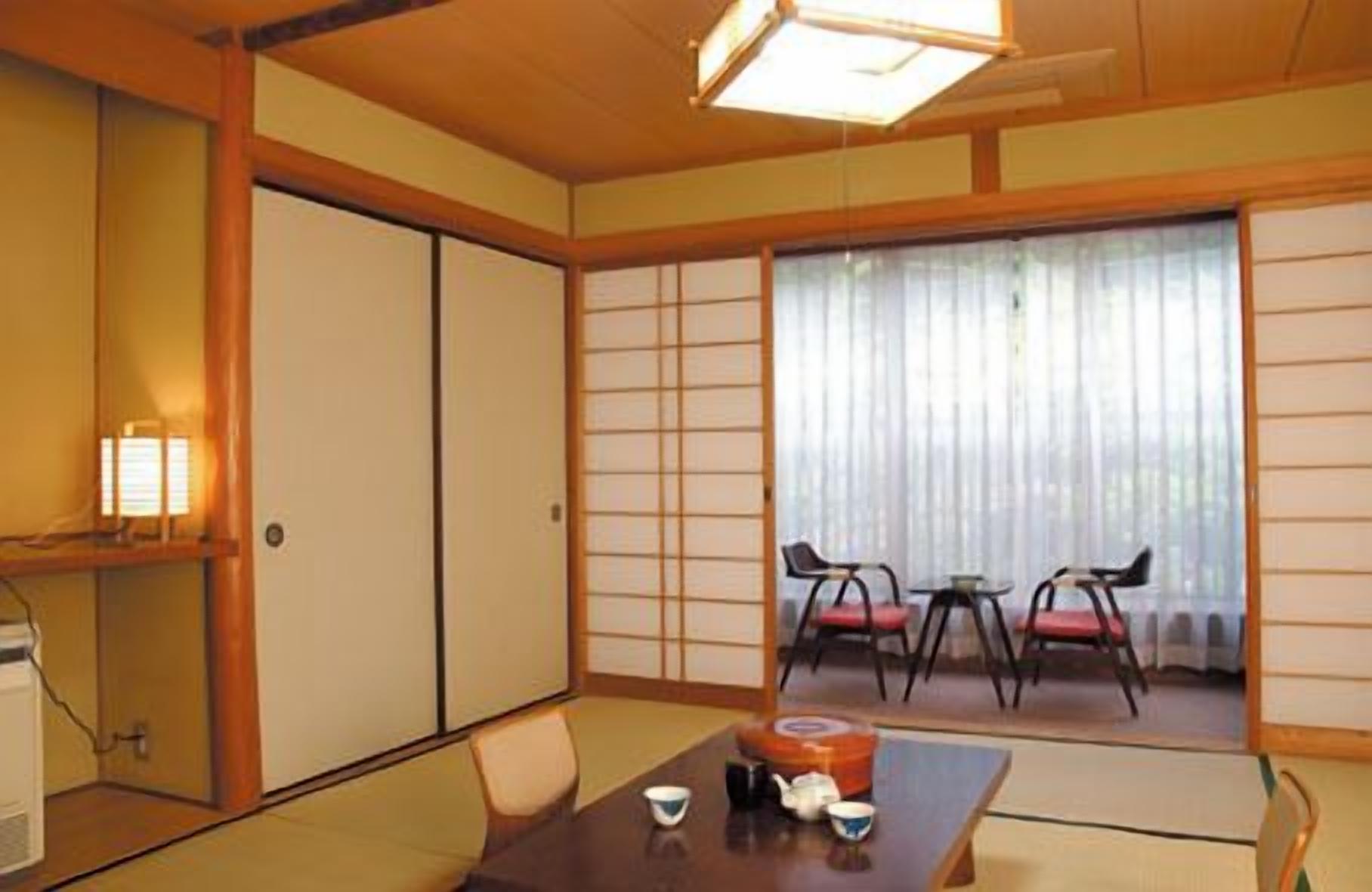Ein traditioneller japanischer Raum mit Tatami-Bodenbelag, Schiebetüren, einem niedrigen Tisch mit Teeservice und Blick durch einen Shoji-Bildschirm.