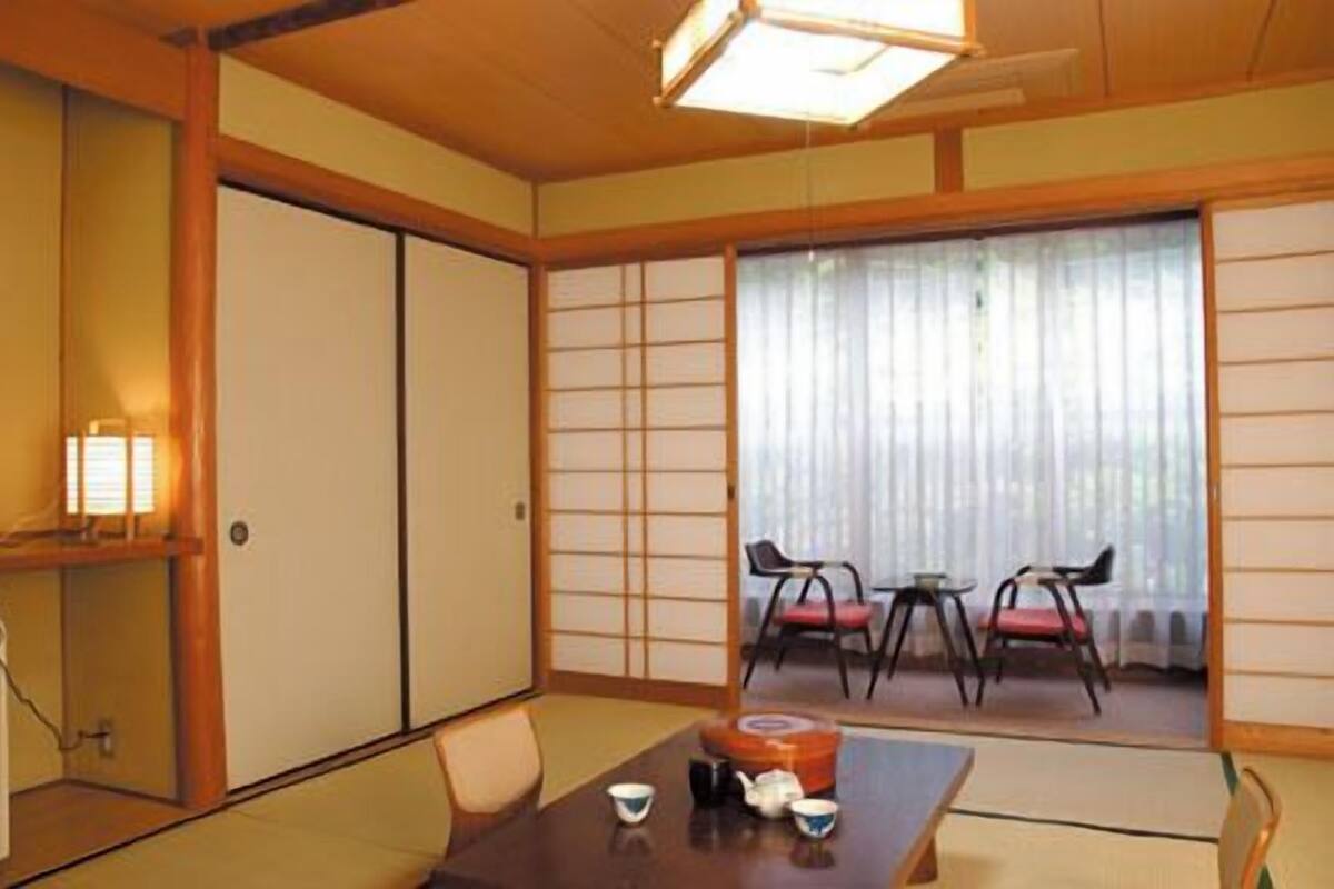 A traditional Japanese room with tatami flooring, sliding doors, a low table with tea set, and a view through a shoji screen.