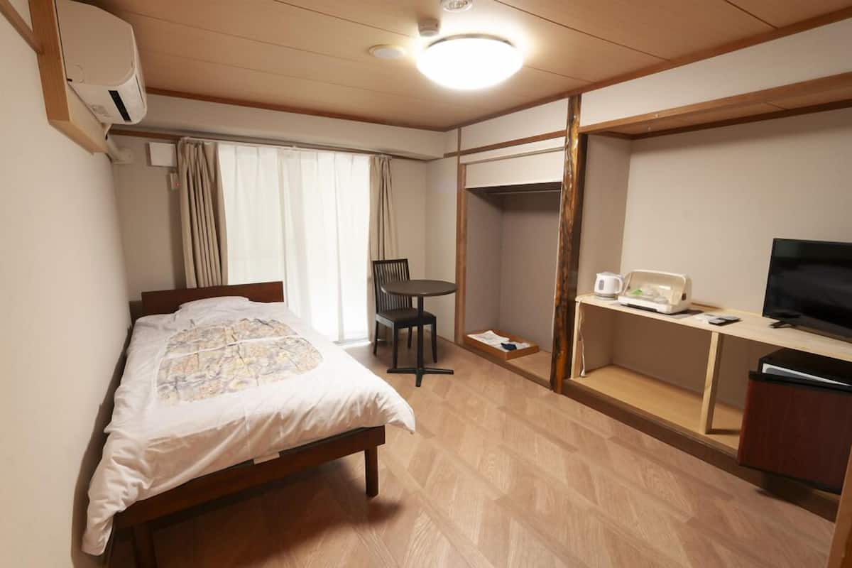 A hotel room with a bed, a desk with a TV, a chair, and a small table.
