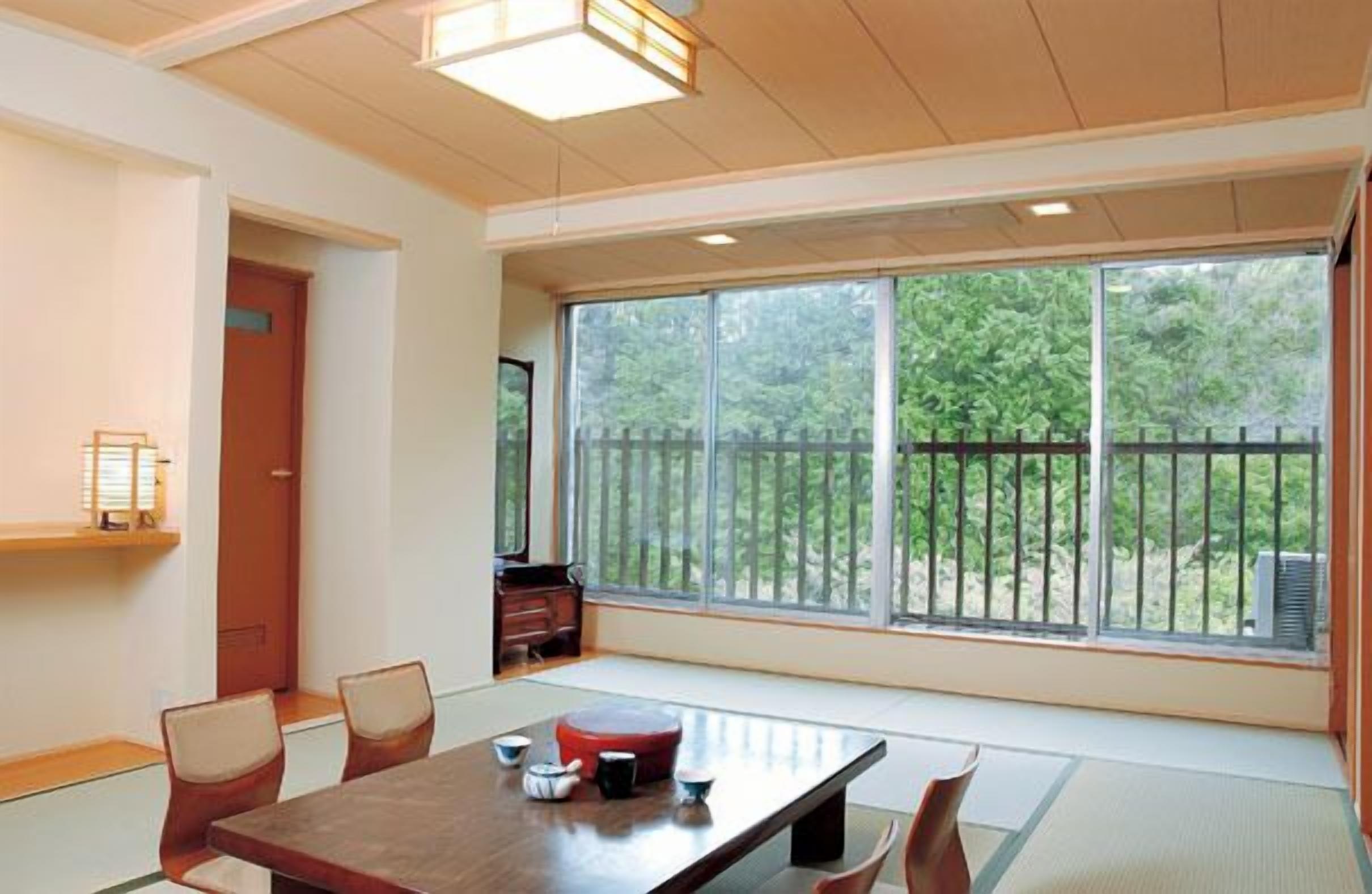A traditional Japanese-style room with tatami flooring, a low table with a red cushion, and a sliding door.