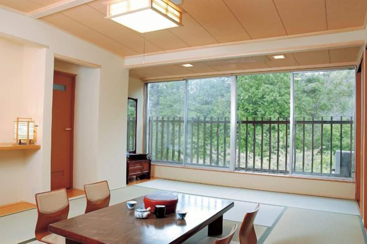 A traditional Japanese-style room with tatami flooring, a low table with a red cushion, and a sliding door.