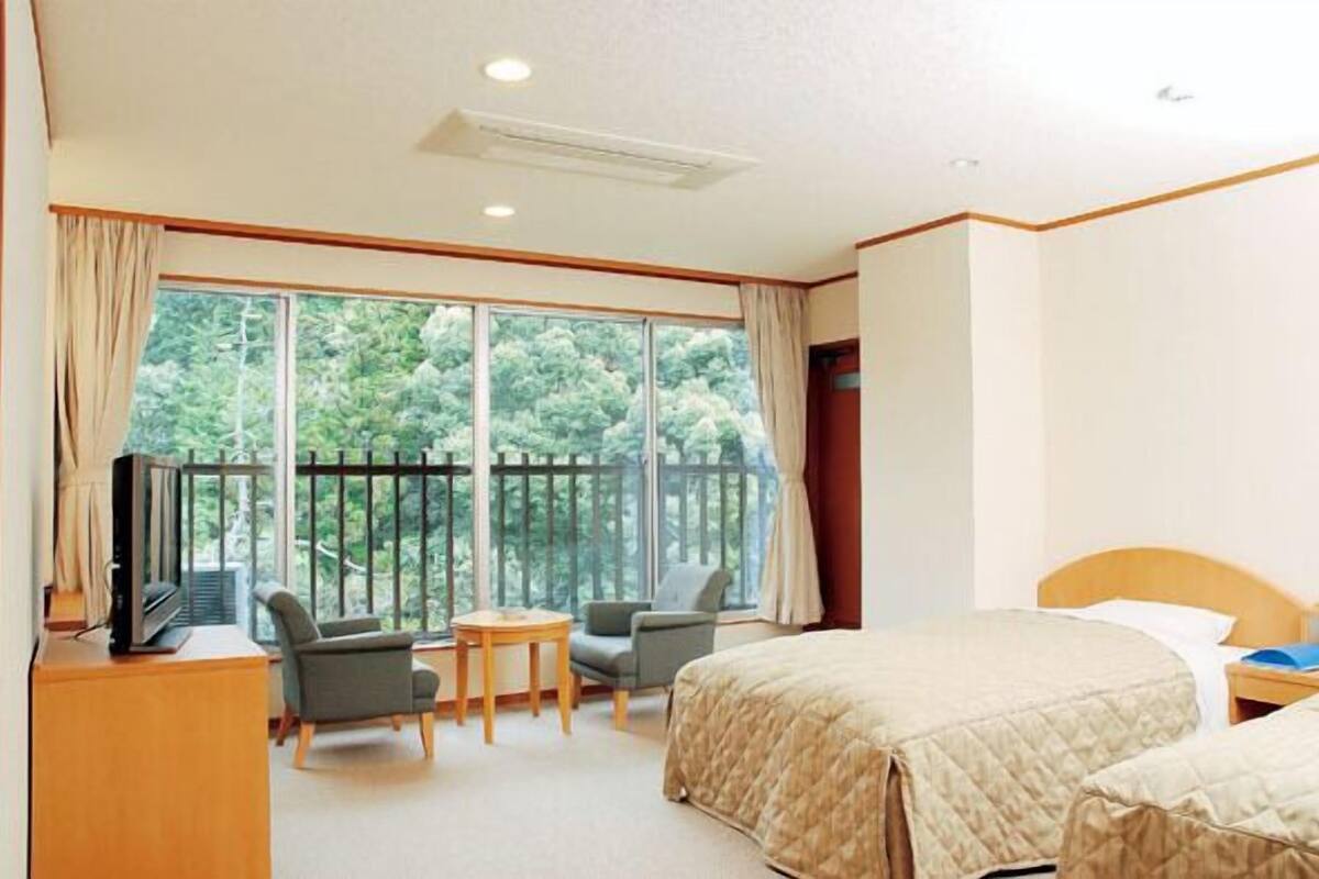 A hotel room with a large window, a bed, a desk with a TV, and two chairs.