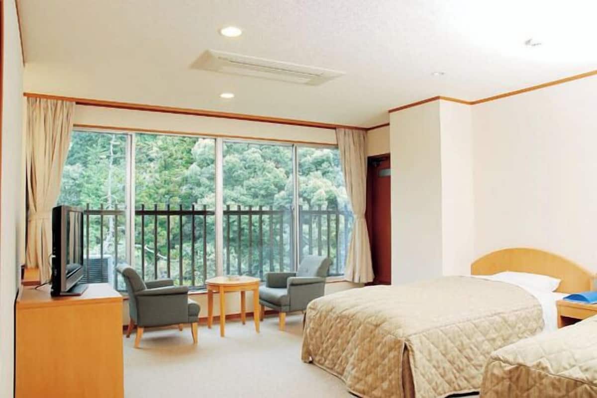 A hotel room with a large window, a bed, a desk with a TV, and two chairs.